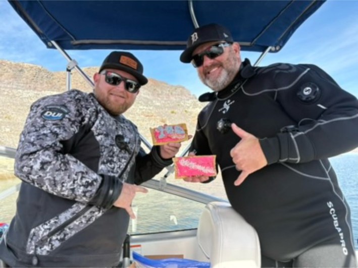 Two divers on a boat at Lake Mead holding homemade sourdough Pop-Tarts to celebrate a 100th dive